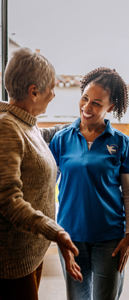 An elderly woman practicing balance exercises with the guidance of a Visiting Angels caregiver, focusing on fall prevention and mobility support.