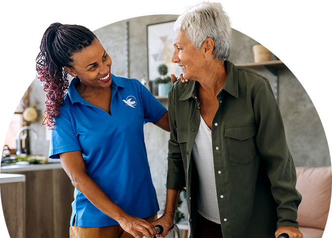 A female Visiting Angels senior home care provider helps a senior woman with her walker.